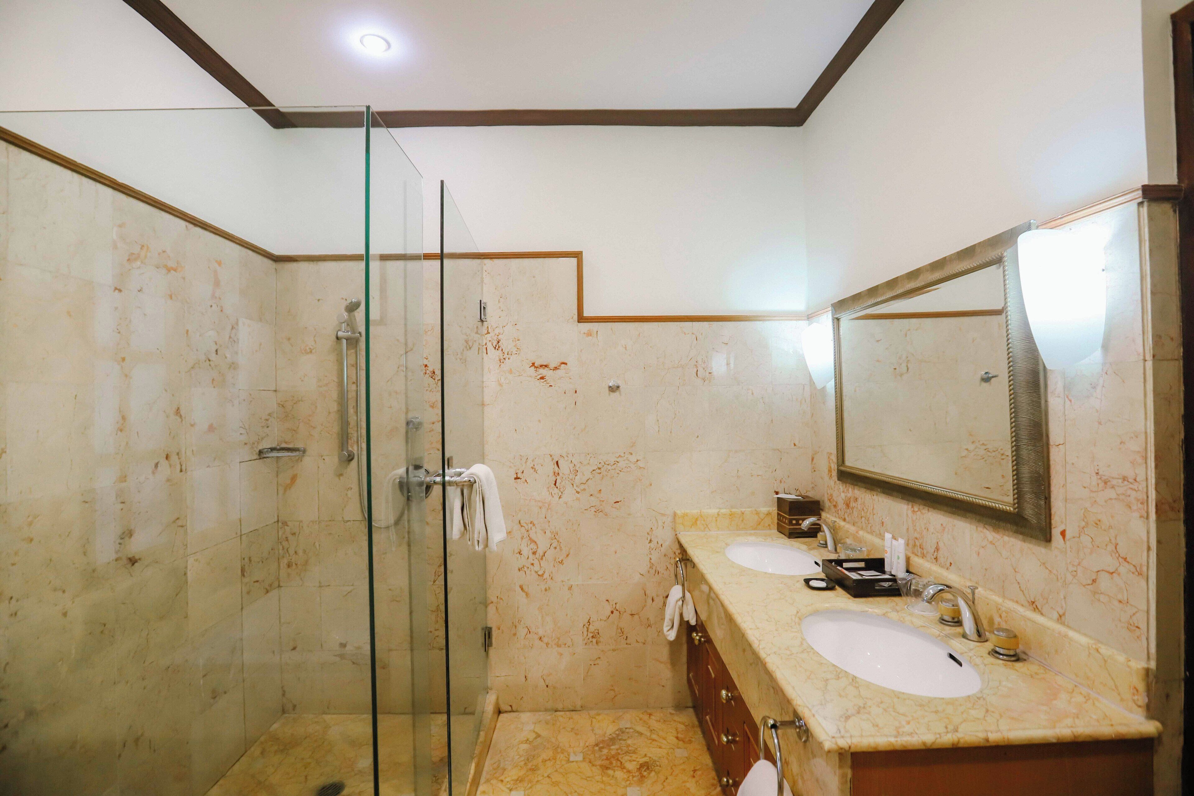 Un baño con cabina de ducha de vidrio, dos lavabos y un espejo grande.