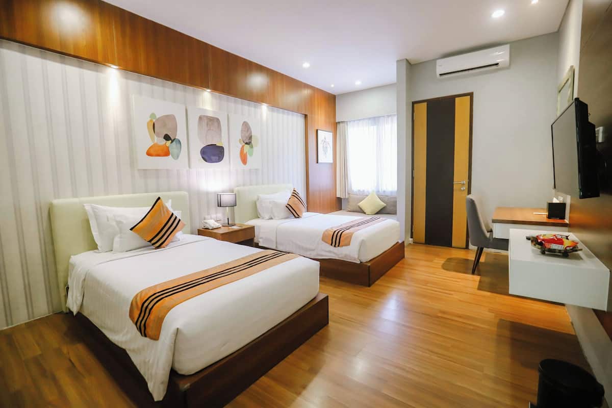 A hotel room with two beds, a desk, a chair, and artwork on the walls.