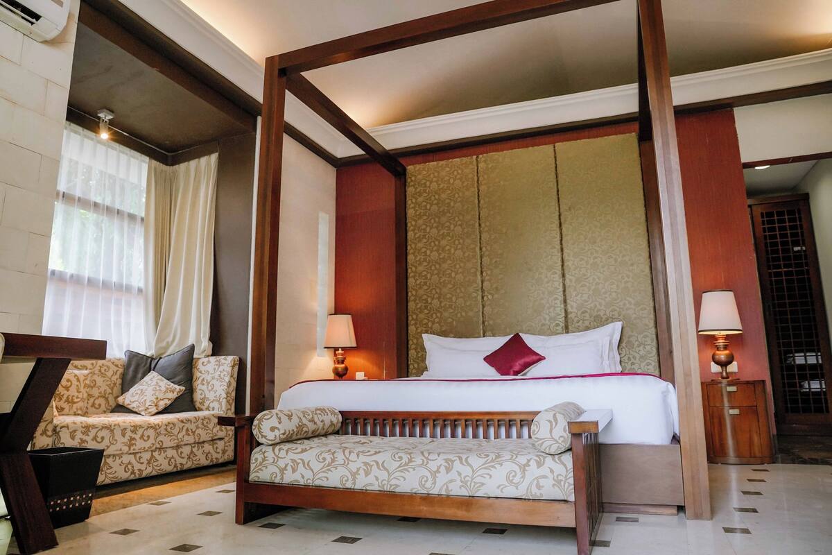 A four-poster bed with a wooden frame, a sofa with patterned cushions, and two bedside tables with lamps.
