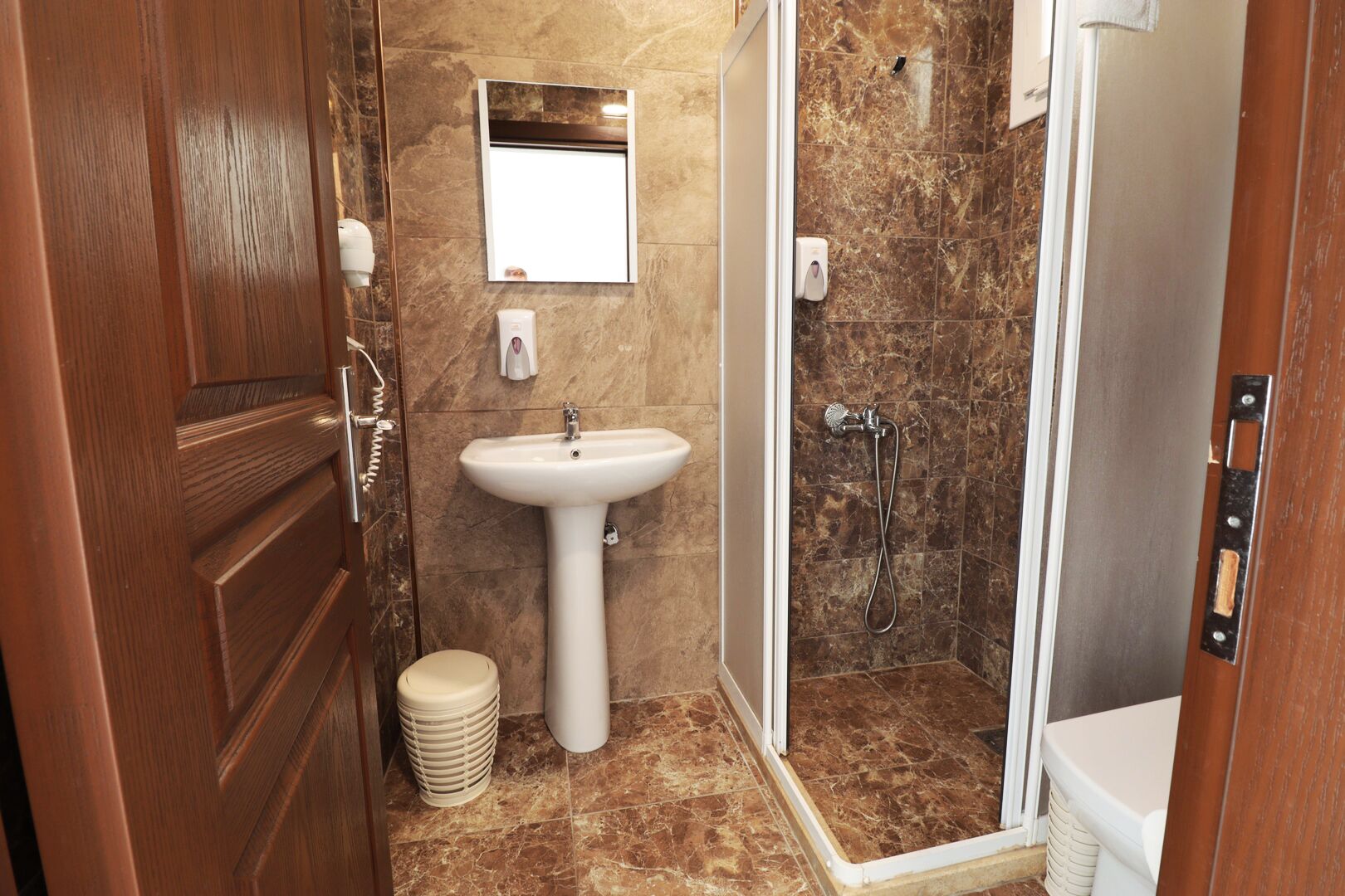 A bathroom with a wooden door, a white sink, a mirror, and a shower area.