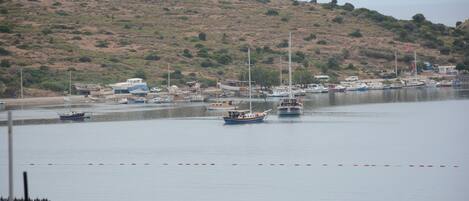 Un puerto deportivo con barcos amarrados, un paisaje montañoso al fondo y un cielo despejado.
