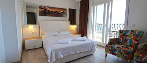 A hotel room with a large bed, two bedside tables, a colorful armchair, and a balcony with a view.