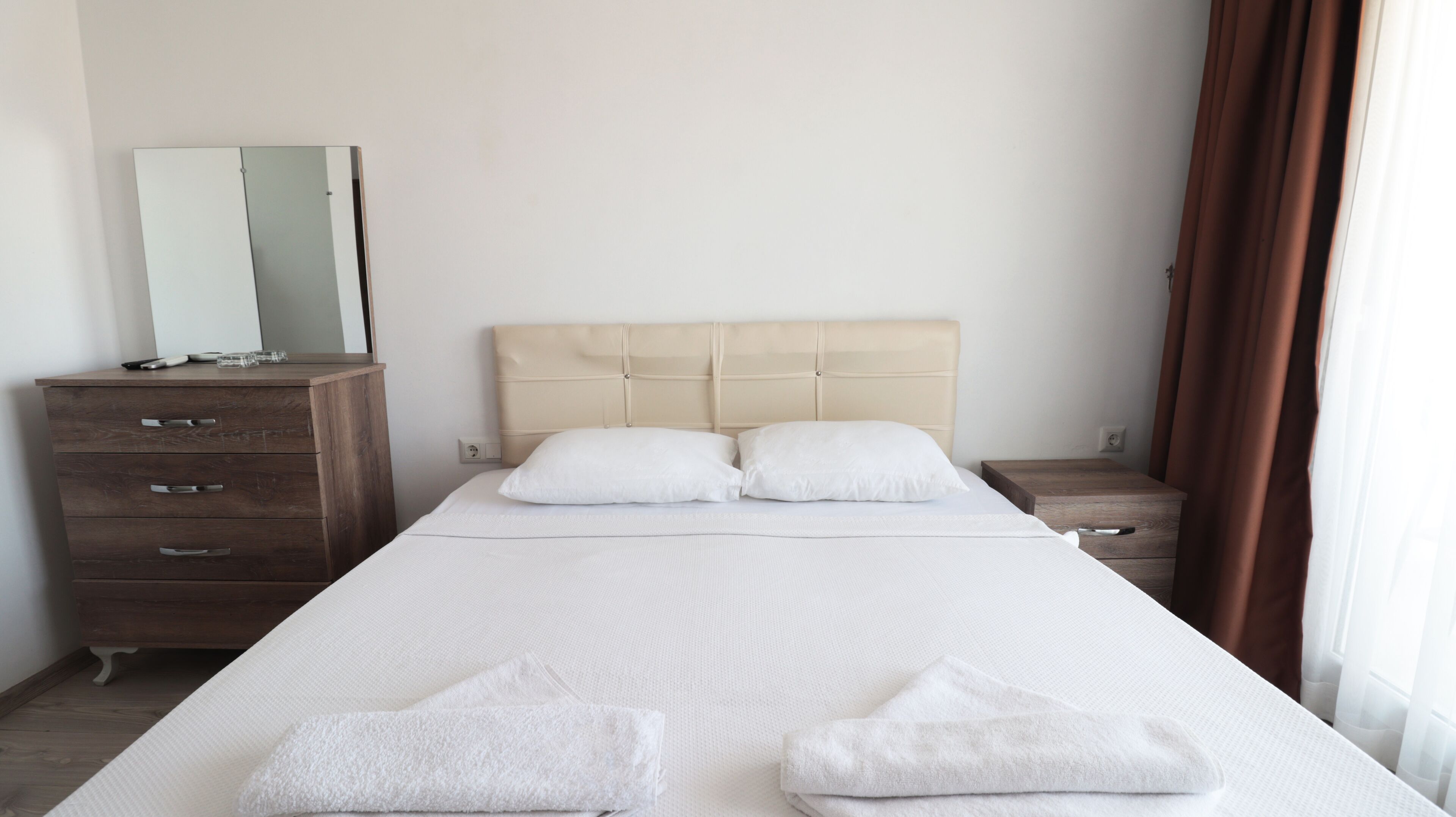 Une chambre d’hôtel avec un grand lit, deux tables de chevet, une commode en bois et un miroir.