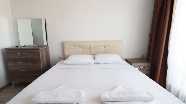 Una habitación de hotel con una cama grande, dos mesitas de noche, un aparador de madera y un espejo.