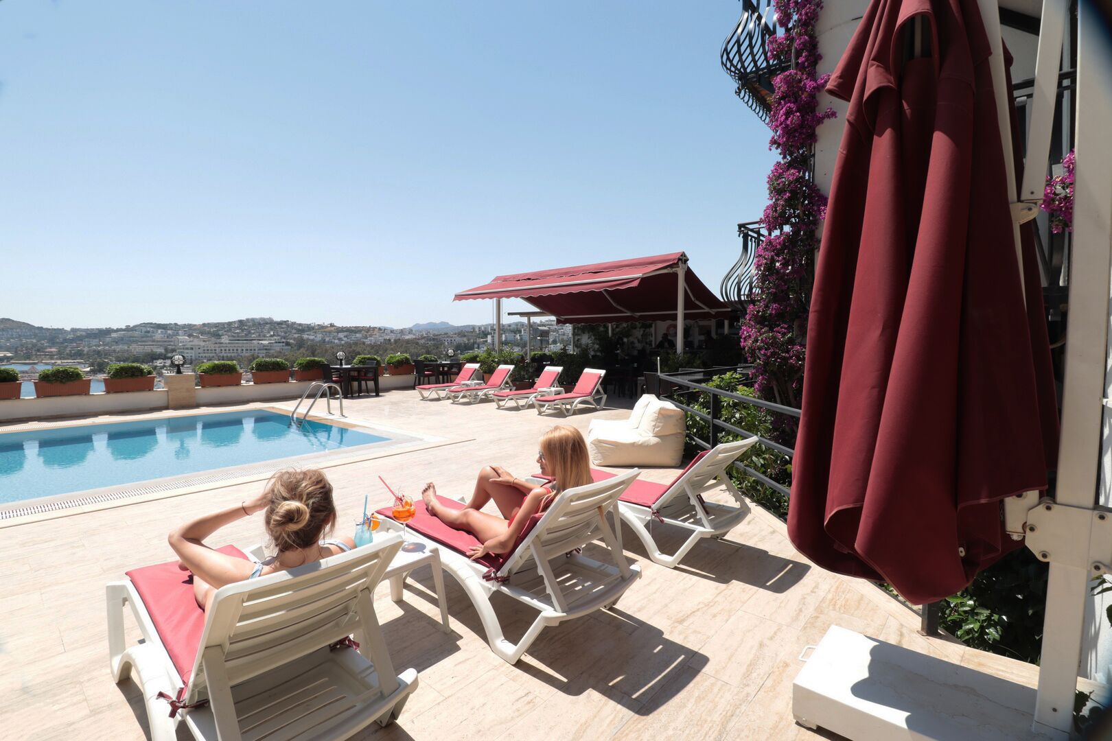 Área de piscina en la azotea con sillones y vistas a la ciudad.