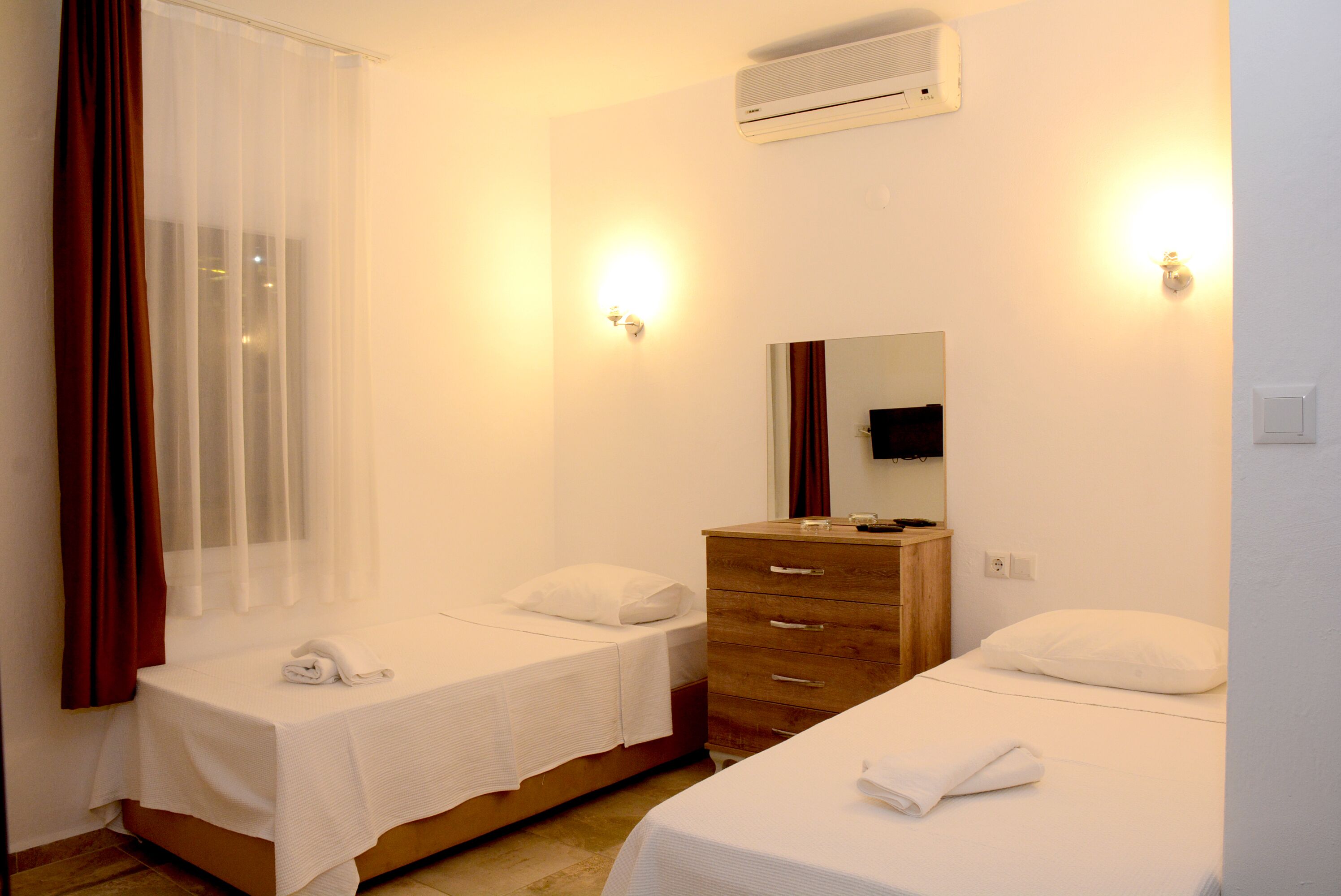 Une chambre d’hôtel avec deux lits, une commode en bois, un miroir et un appareil de climatisation.