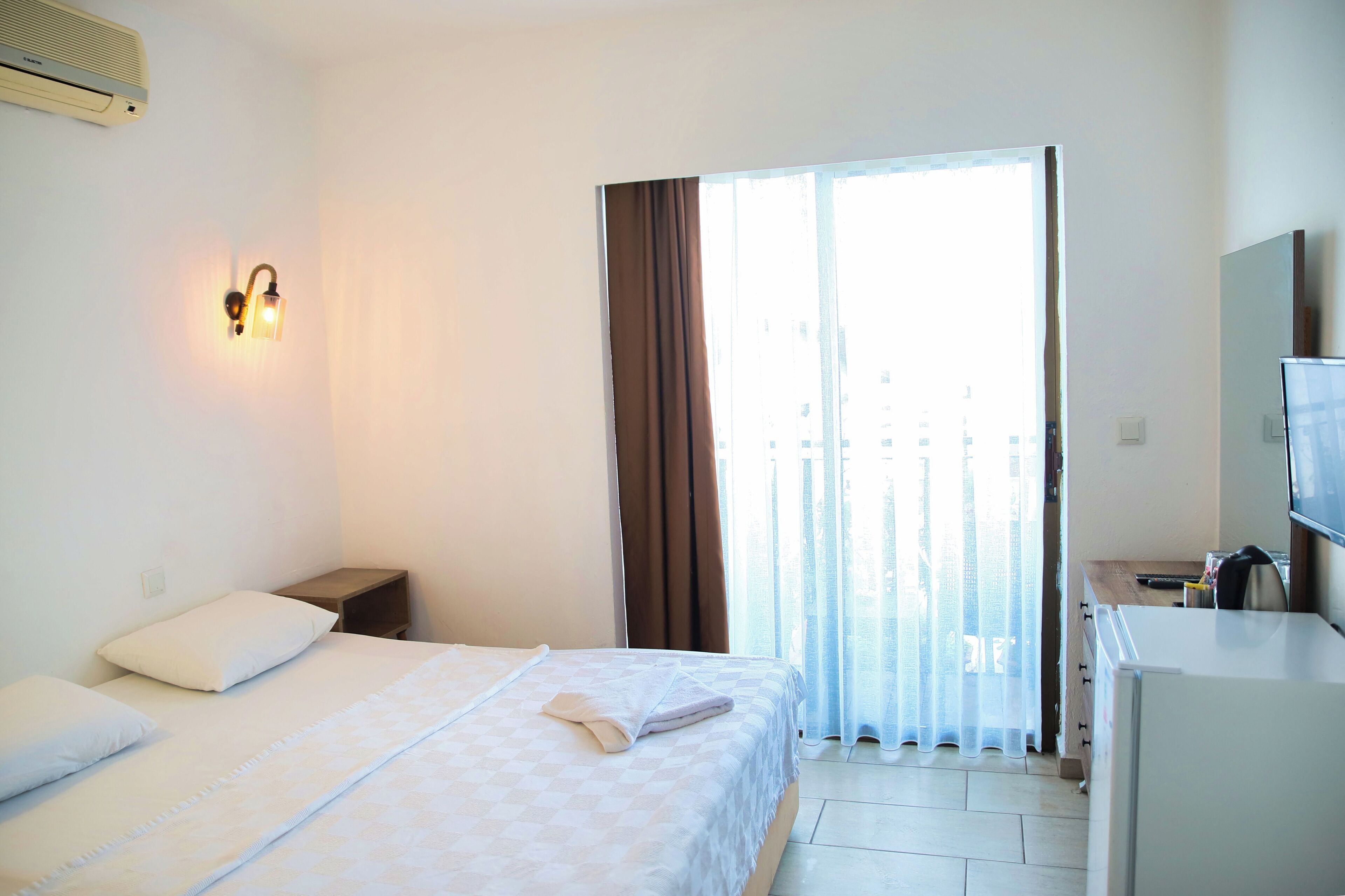Habitación de hotel con cama, mesita de noche, televisor y vistas a través de una ventana con cortinas.