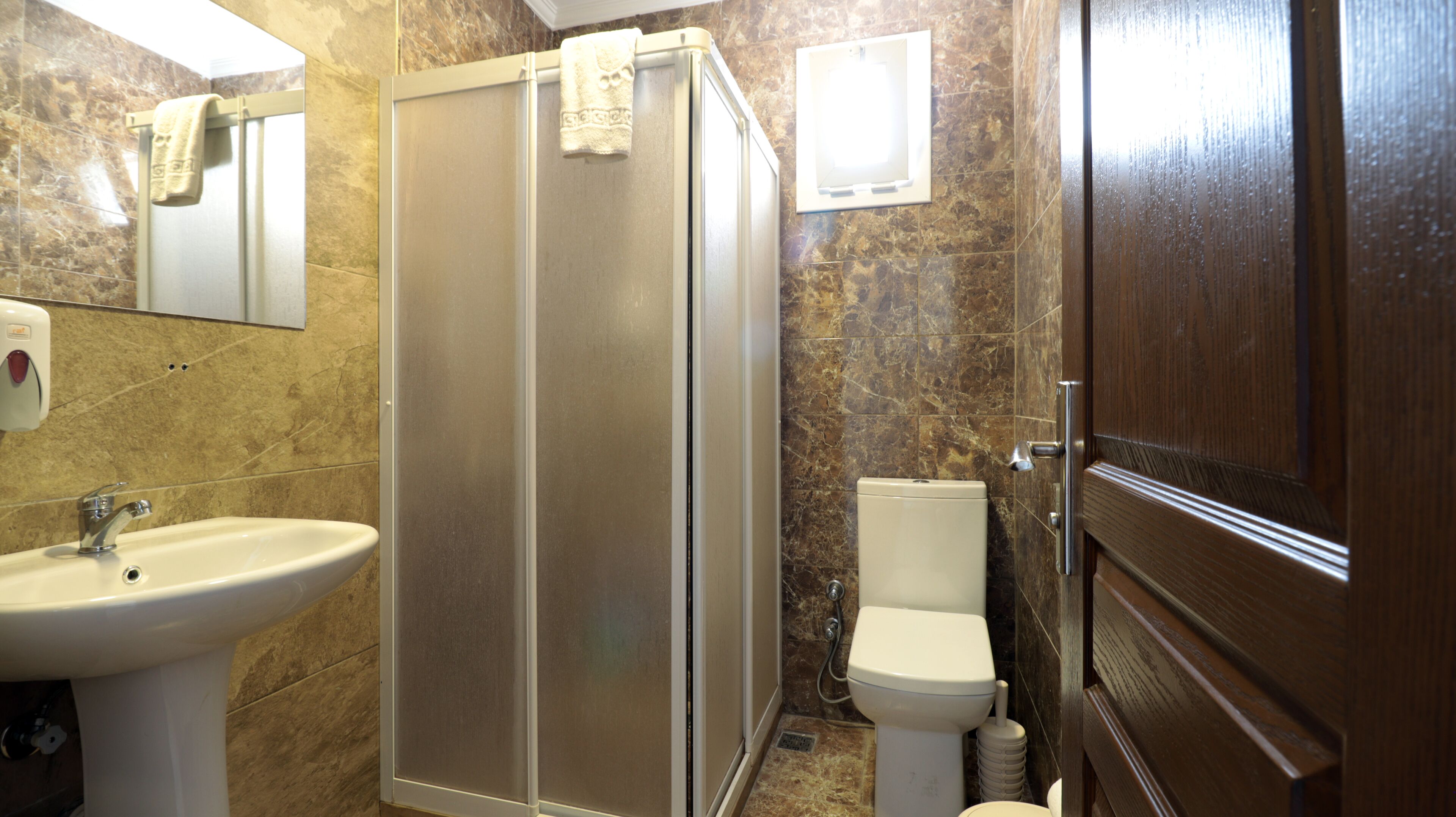Un baño con ducha, lavabo, inodoro y puerta de madera.