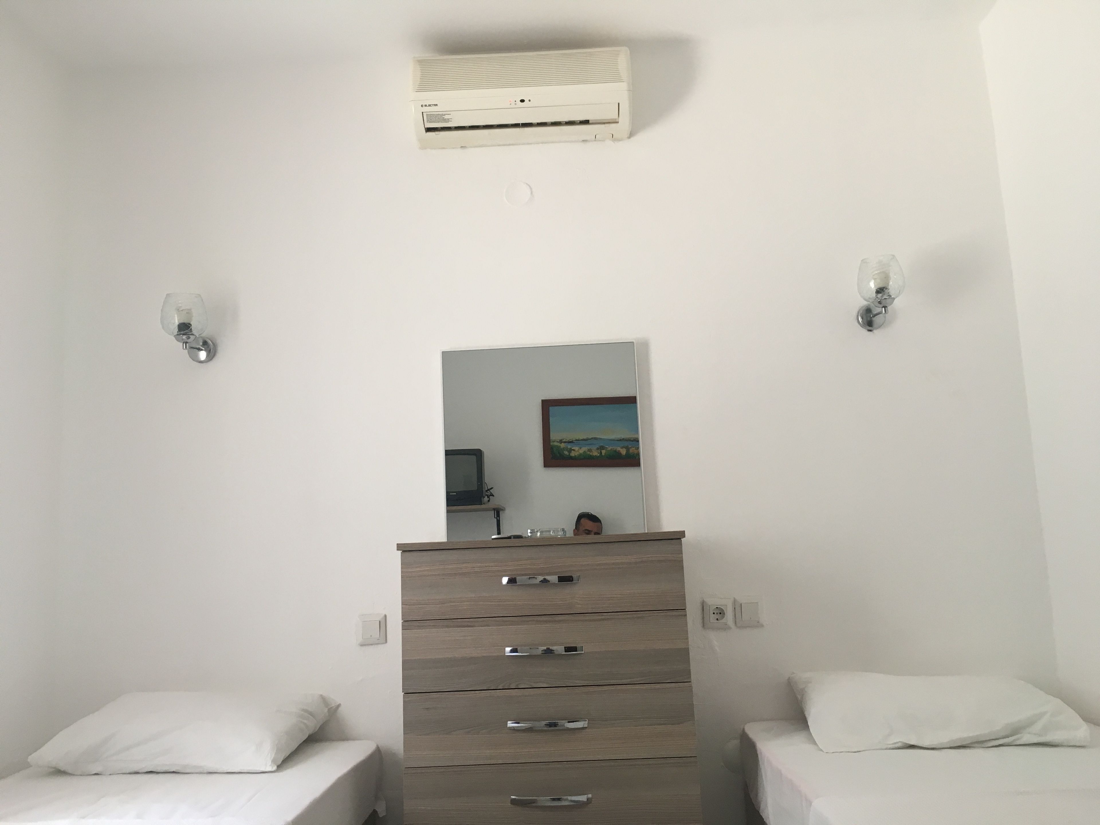 Un dormitorio con dos camas individuales, un aparador de madera, un aire acondicionado instalado en la pared y un cuadro.