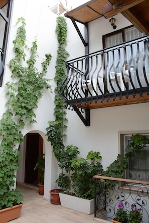Un patio con plantas en macetas, una puerta de madera y un balcón con barandilla de hierro forjado.