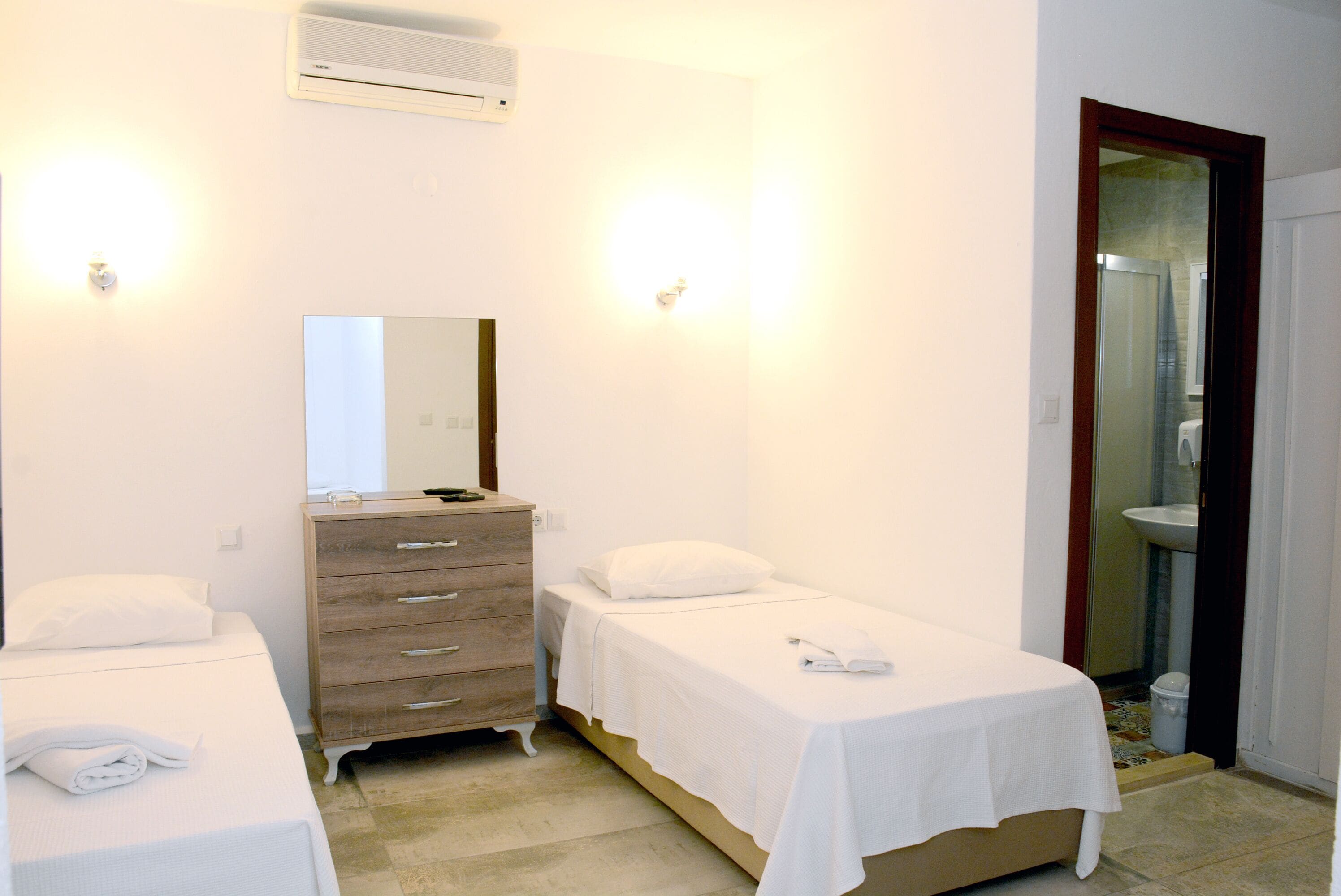 A hotel room with two single beds, a wooden dresser, a mirror, and a bathroom with a sink and shower.