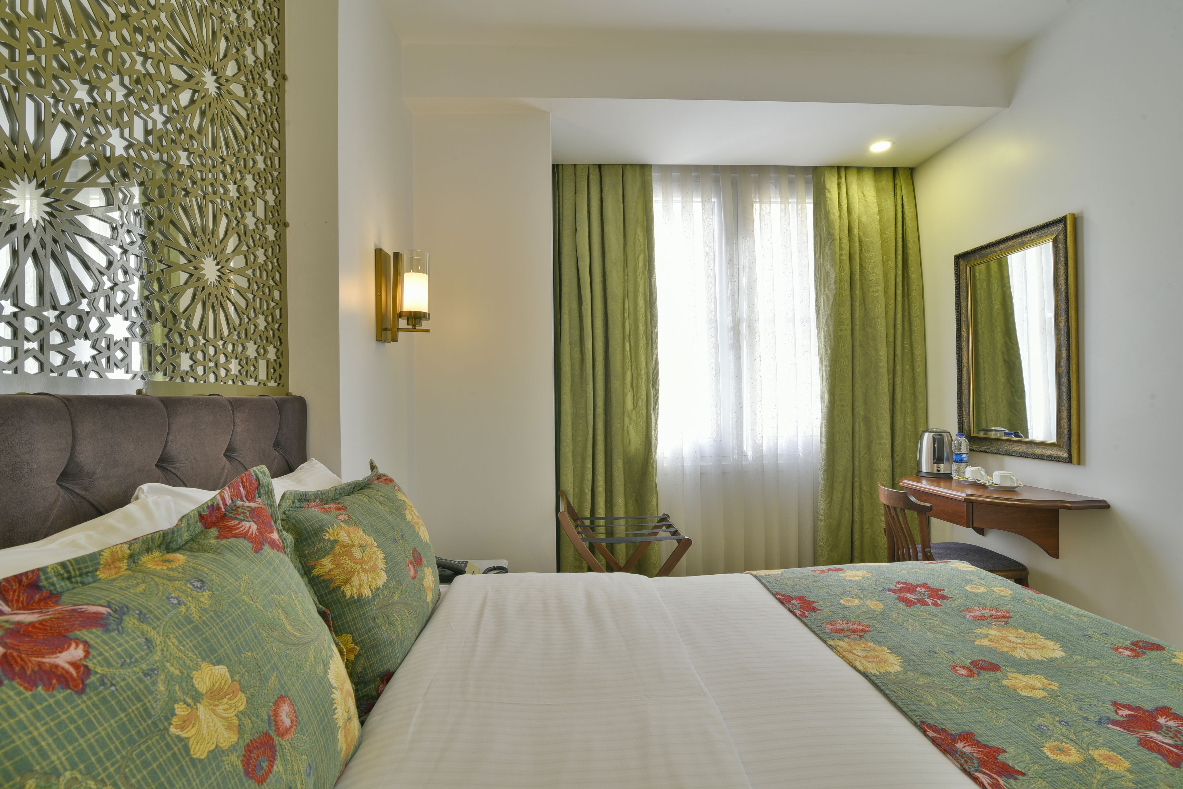 A hotel room with a bed, a desk, a chair, a decorative wall panel, and a mirror.