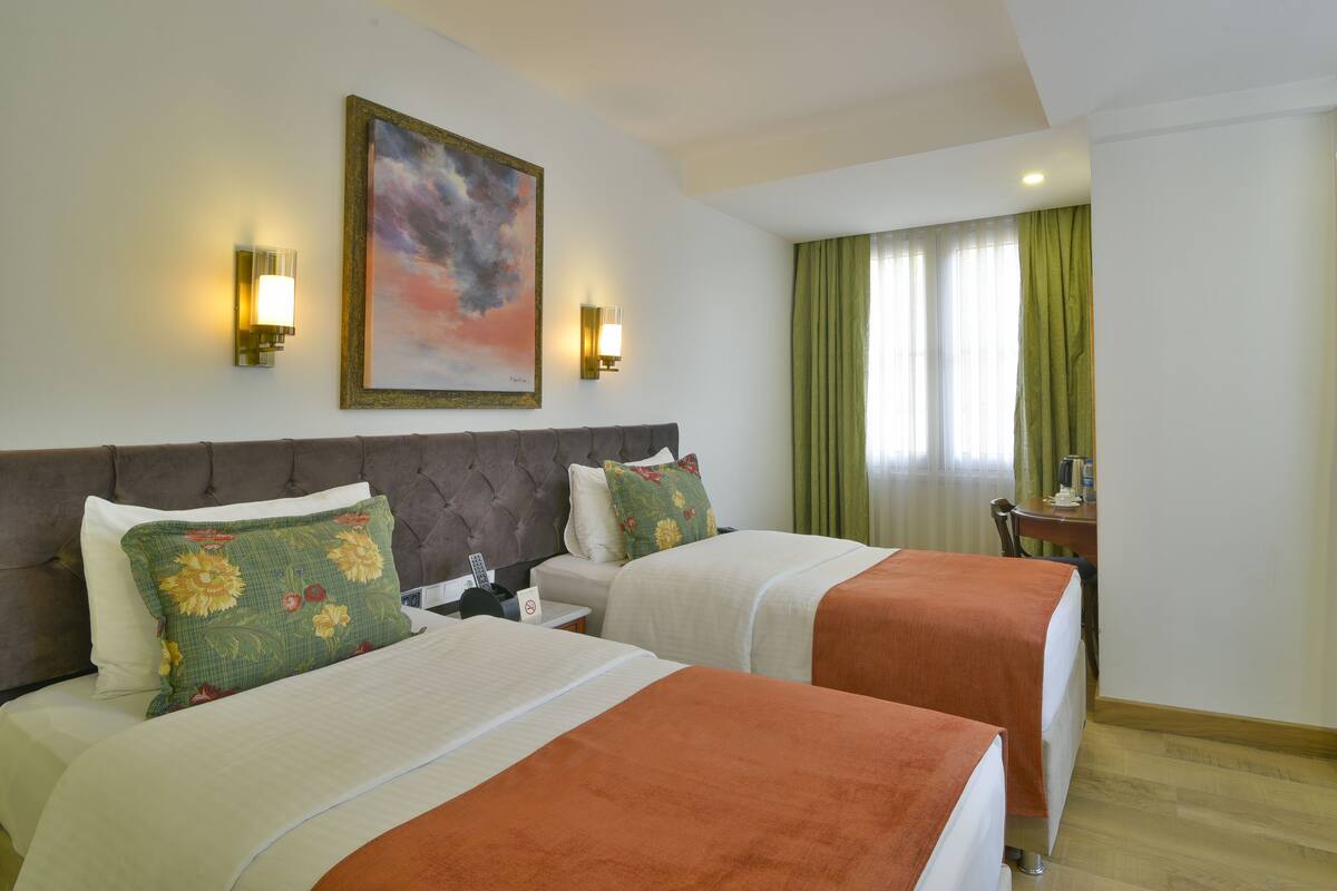 A hotel room with two beds, a large painting on the wall, and a desk with a chair.