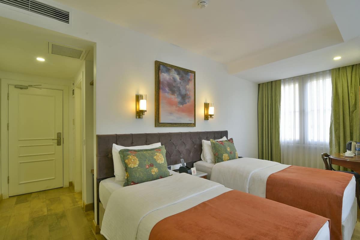A hotel room with two beds, a painting on the wall, and a view of the outdoors.