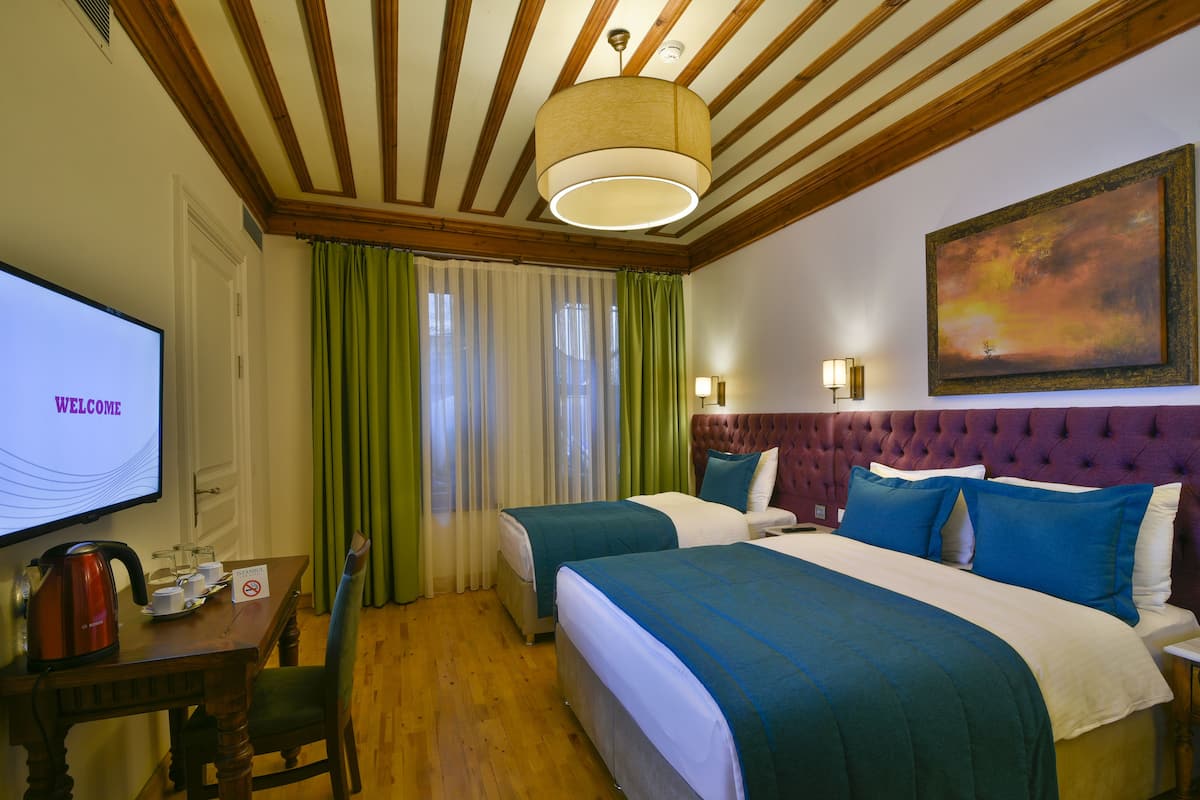 A hotel room with two beds, a television, a desk with a kettle, and a painting on the wall.