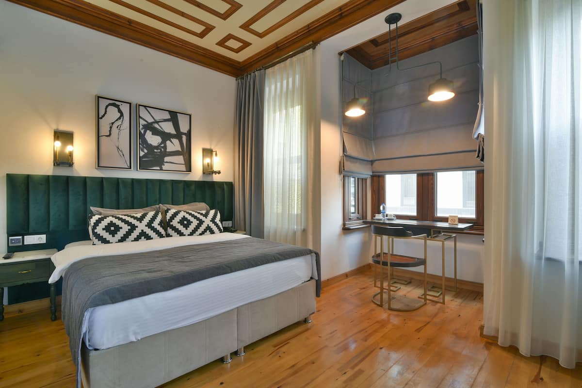 A bedroom with a large bed, a desk, and a window with curtains.