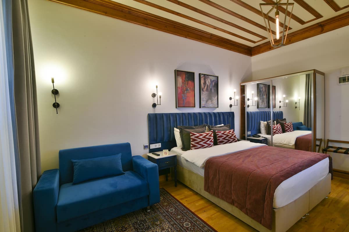 A bedroom with a bed, a blue sofa, a nightstand, and a mirror.