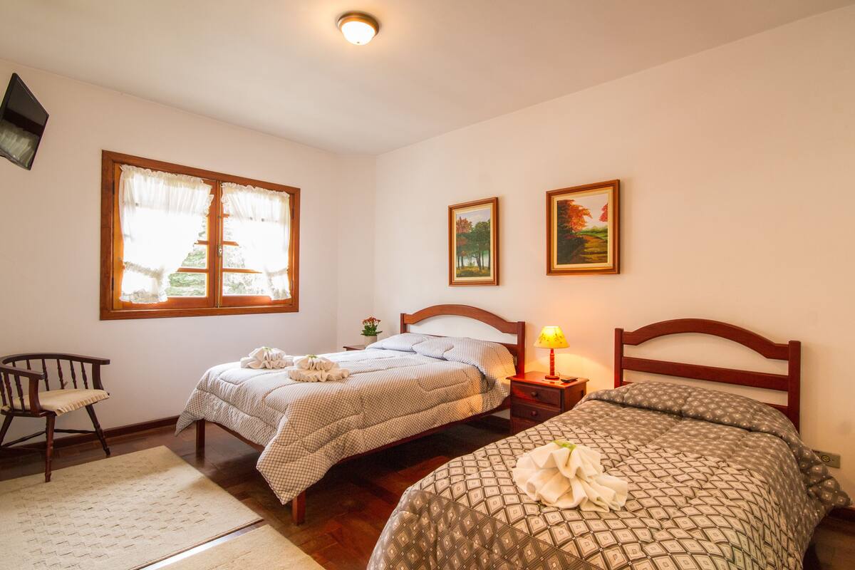 Ein Schlafzimmer mit zwei Betten, einem Holzstuhl, einem Nachttisch mit Lampe sowie zwei gerahmten Bildern an der Wand.