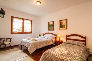 A bedroom with two beds, a wooden chair, a nightstand with a lamp, and two framed pictures on the wall. - Pousada Serena (Campos do Jordão)