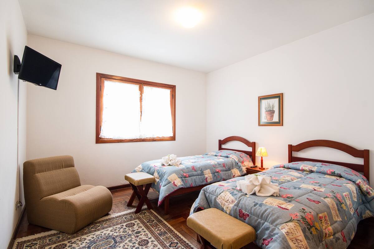 Ein Schlafzimmer mit zwei Betten, einem Sessel, einem Fernseher und einem Fenster.