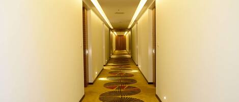 A long, narrow hotel corridor with a patterned carpet and overhead lighting.