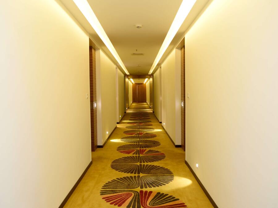 A long, narrow hotel corridor with a patterned carpet and overhead lighting.