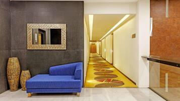 Un hall de hotel con un sofá azul, un espejo grande y dos jarrones.