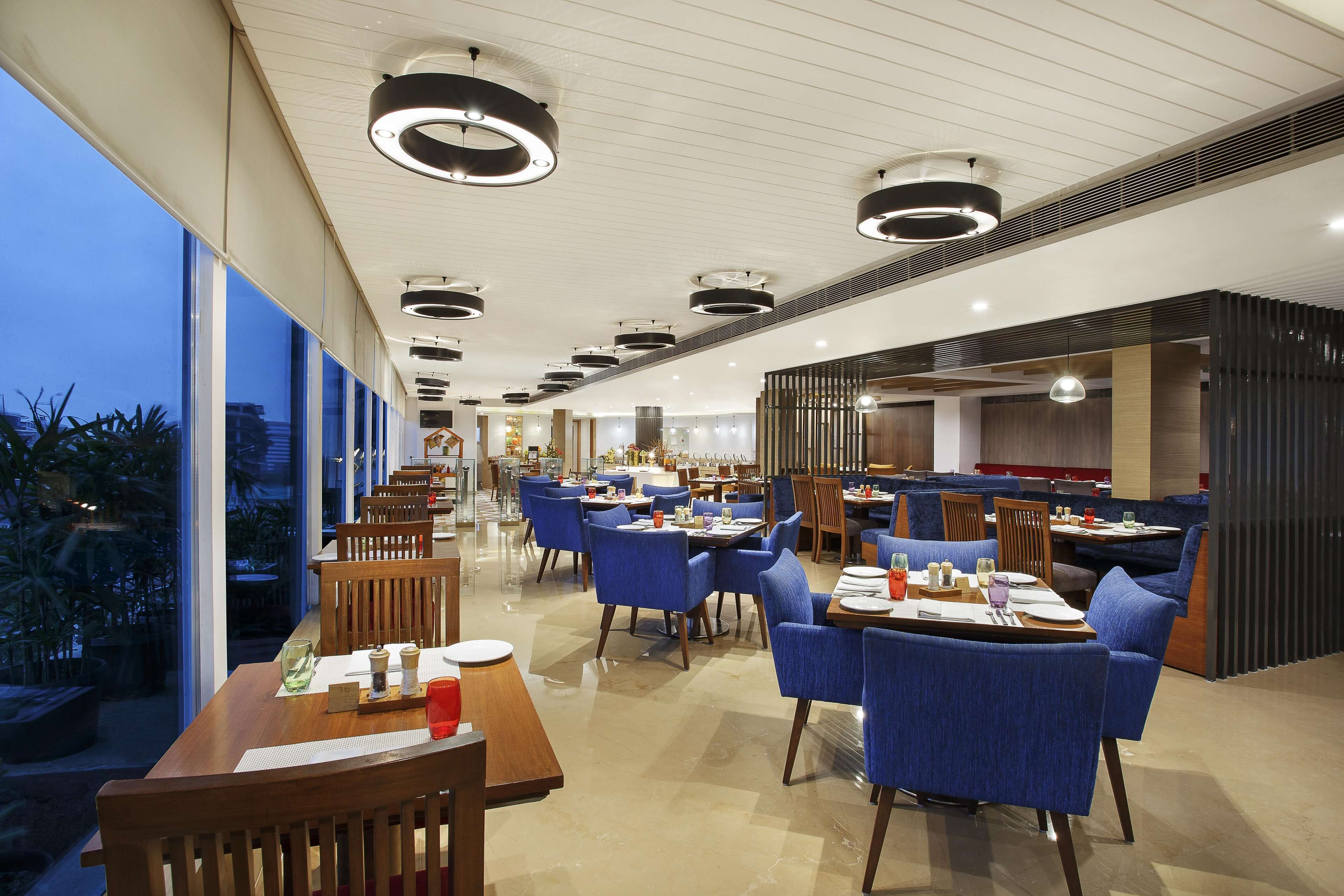 A modern restaurant with high ceilings, pendant lighting, and a mix of wooden and upholstered chairs.