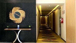A hotel lobby with a reception desk, a decorative wall piece, a patterned carpet, and a hallway leading to rooms.