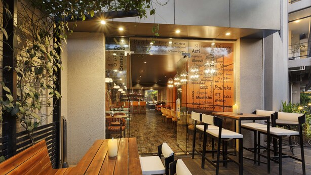 An outdoor dining area with wooden tables and benches, a brick wall with climbing plants, and a menu board with various food and drink options.