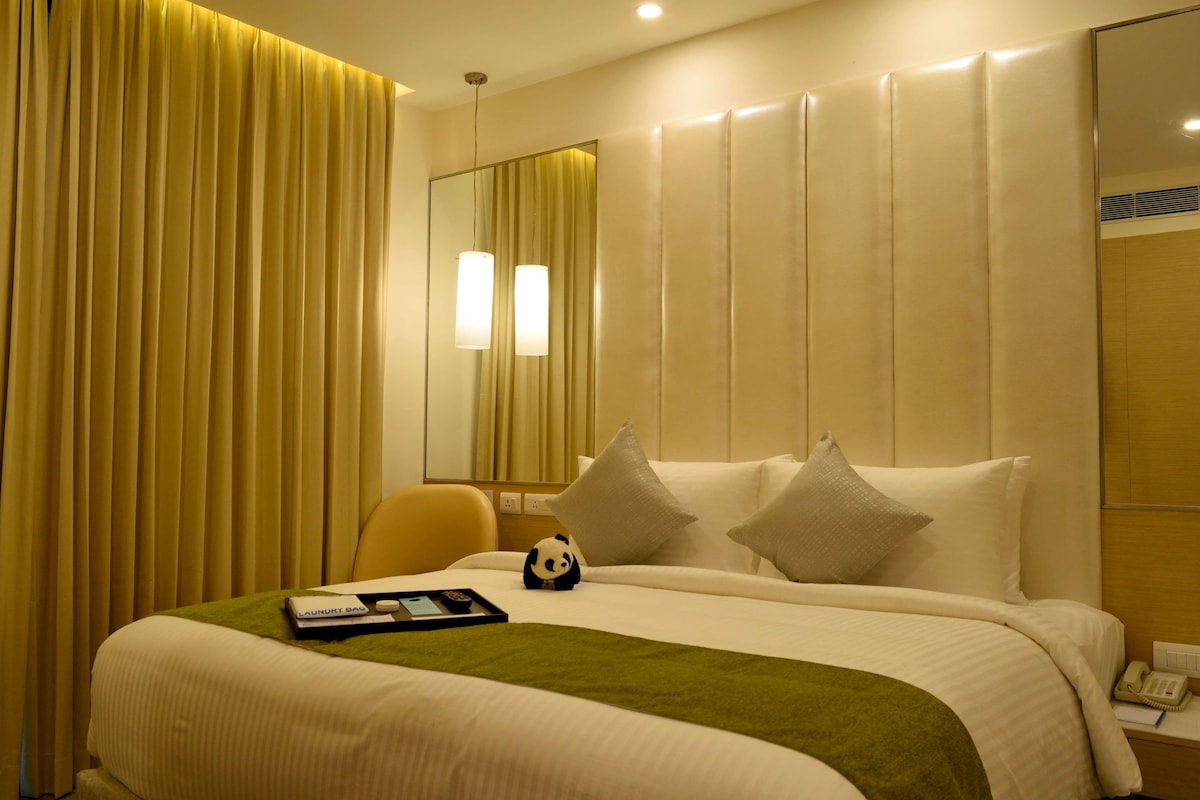 Una habitación de hotel con cama, una silla, mesita de noche con teléfono y un espejo.