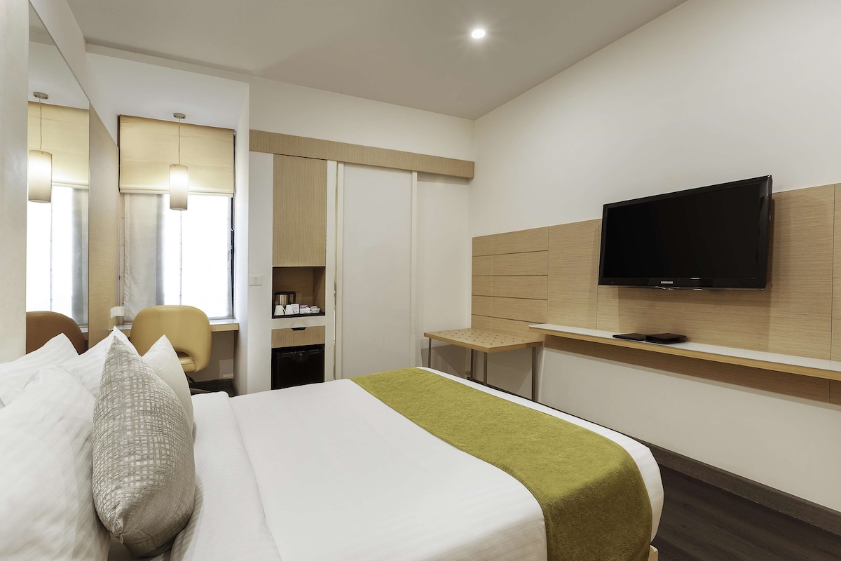 Una habitación de hotel con una cama, televisión montada en la pared, un escritorio y una silla.