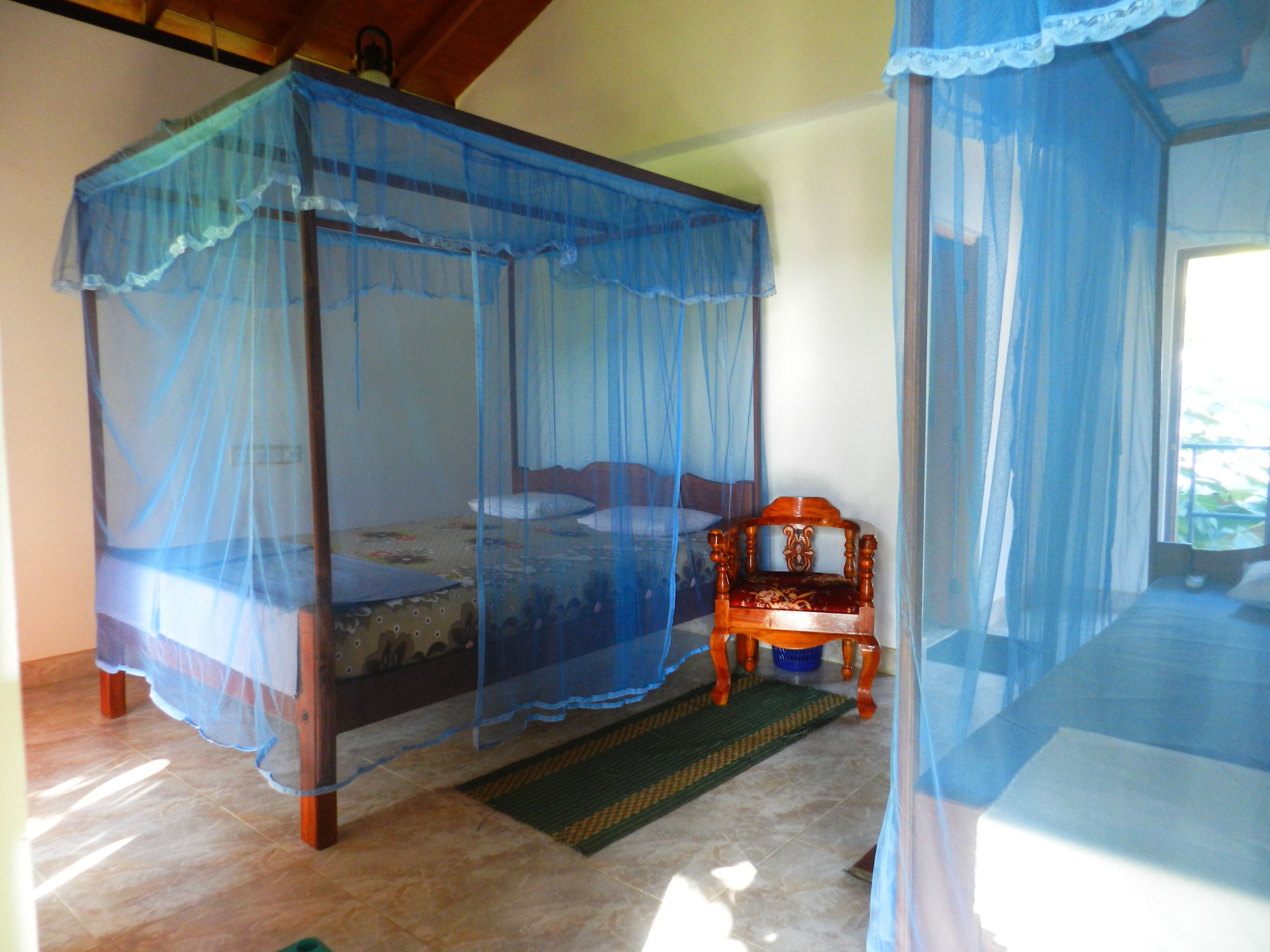 A room with a four-poster bed, a wooden chair, and a mosquito net.