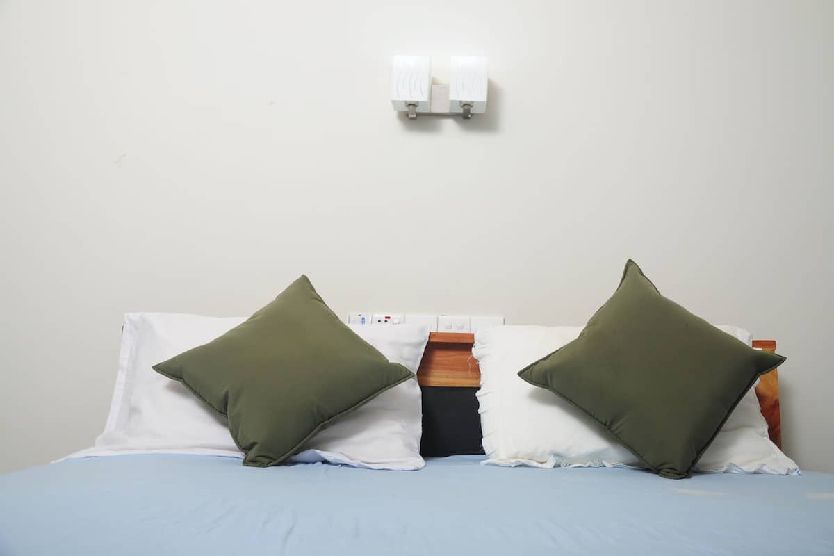 Una cama con dos almohadas, un cabecero de madera y una lámpara fijada a la pared.