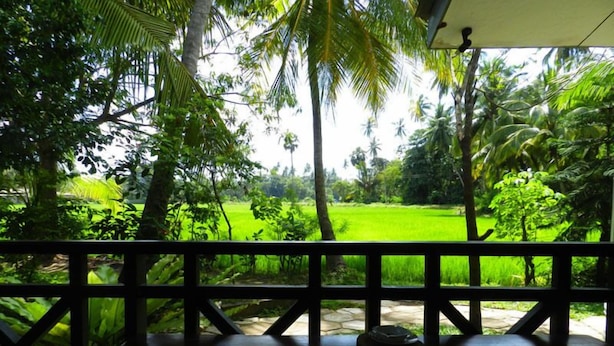 A wooden table with a tire in the center, surrounded by a railing, overlooking a lush green field and palm trees. - Traveller's Home Hotel (Thissamaharama)