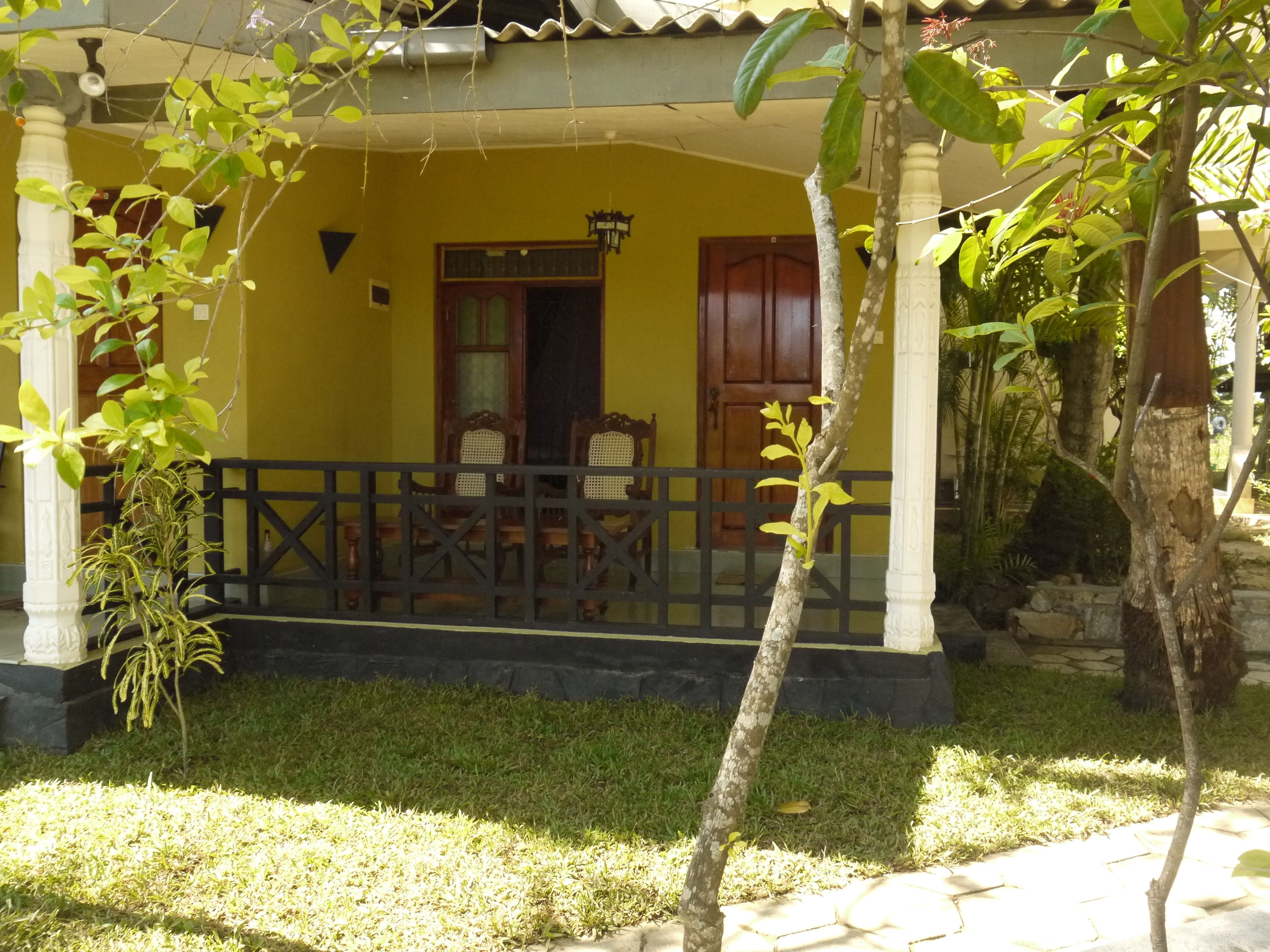 A yellow building with a porch, a wooden door, and a small table with chairs.