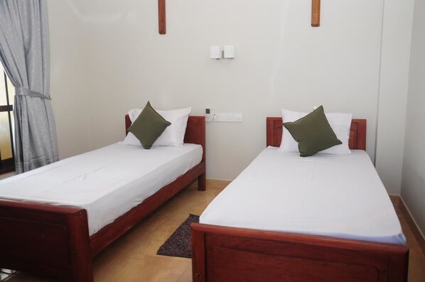 Two single beds with wooden frames and white linens, each with a green pillow.