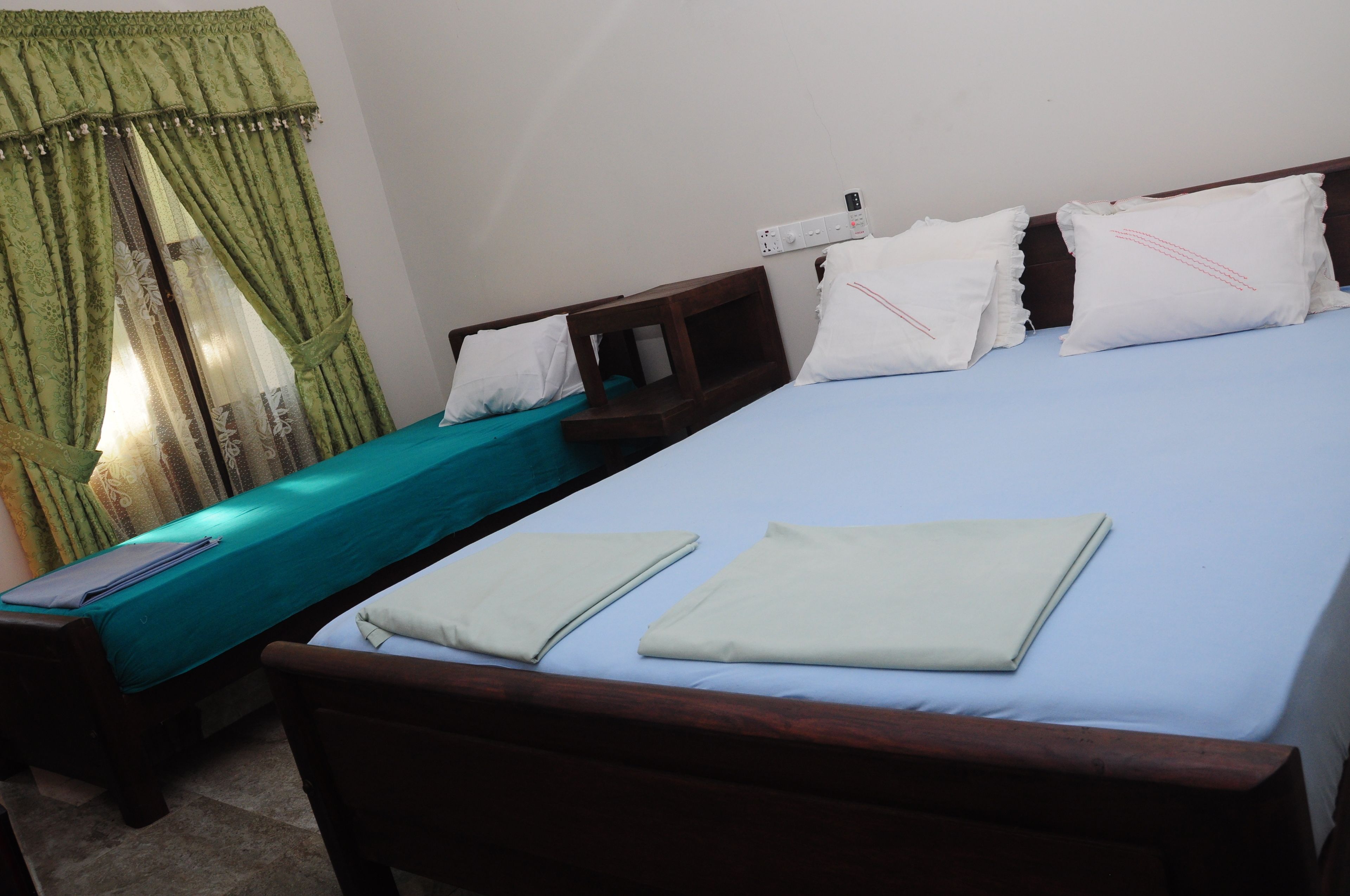 A bedroom with a single bed, a wooden nightstand, a green curtain, and a white pillow.