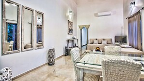 A modern living room with a glass coffee table, a sofa, and a television. There are three large mirrors on the wall and an air conditioning unit above the sofa. - Maya's Residence (Rethymno)