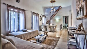 A spacious living room with a high ceiling, a dining area, and a staircase leading to an upper floor. - Maya's Residence (Rethymno)