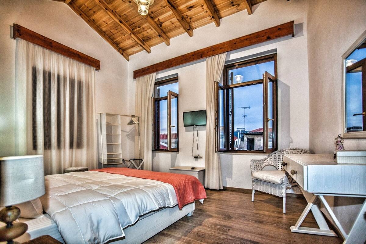 A bedroom with a bed, a desk, a chair, and large windows.