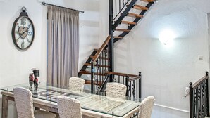 A dining area with a glass table, four chairs, a clock, and a staircase. - Maya's Residence (Rethymno)