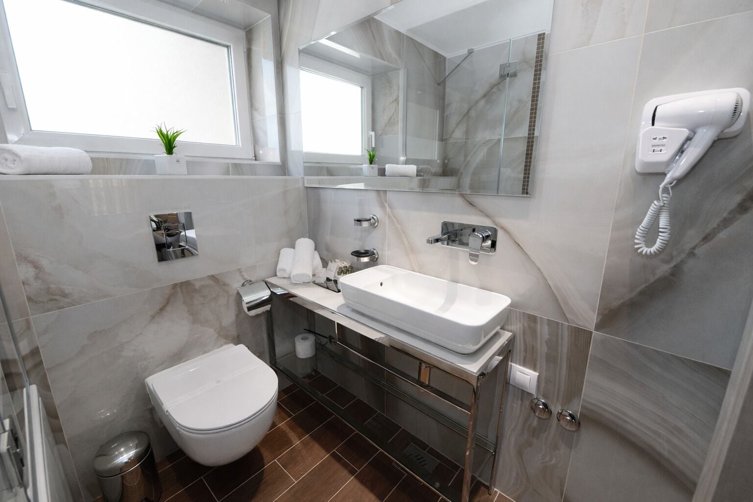 A modern bathroom with a white sink, a toilet, a shower, and a hairdryer on the wall.