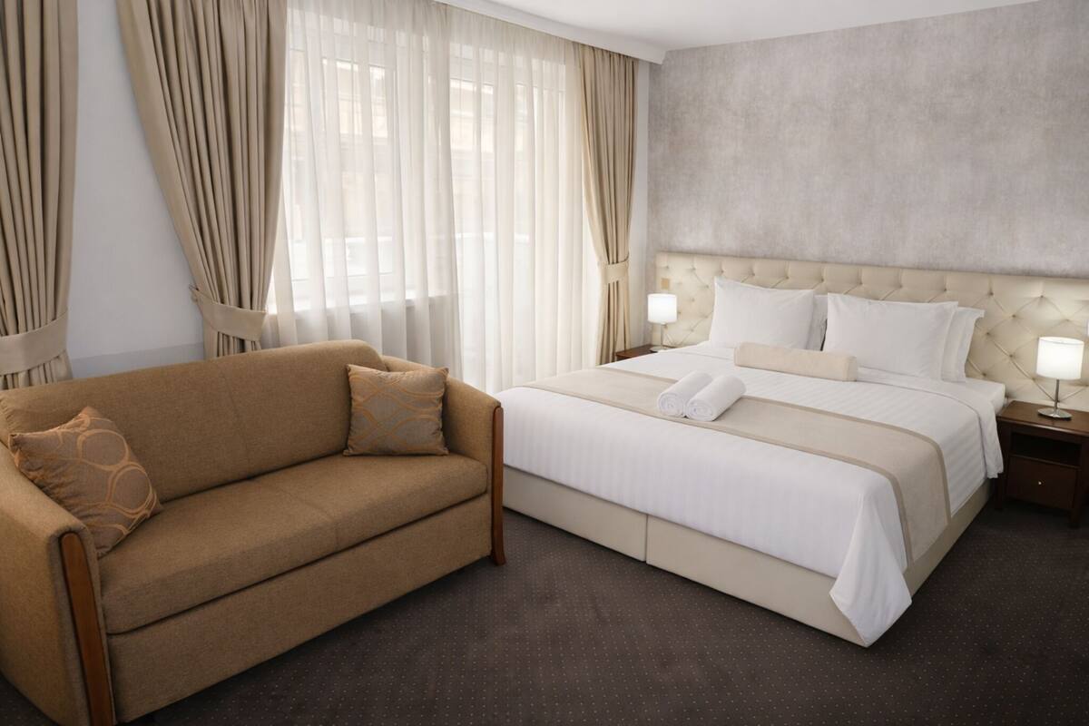 Une chambre d’hôtel avec un lit, un canapé, des rideaux, une table de chevet et une lampe.
