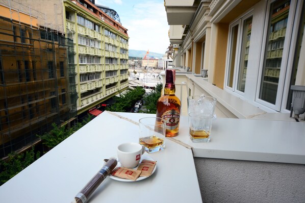 Un balcón con una botella de Chivas Regal, dos vasos, una taza y un cigarro sobre una mesa blanca.