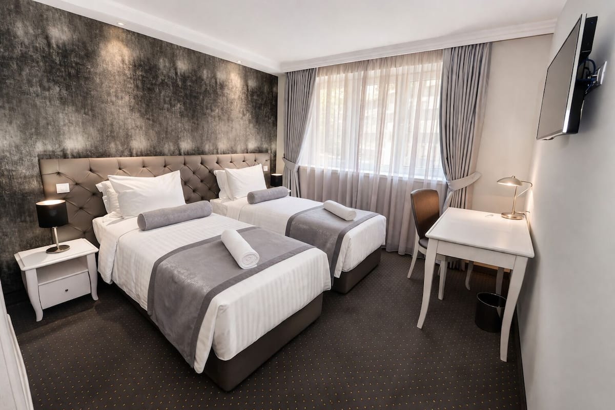Une chambre d’hôtel avec deux lits, un bureau, une chaise, une télévision et une grande fenêtre avec des rideaux.