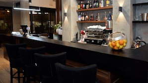 A modern bar area with a long counter, bar stools, a coffee machine, and shelves stocked with bottles.