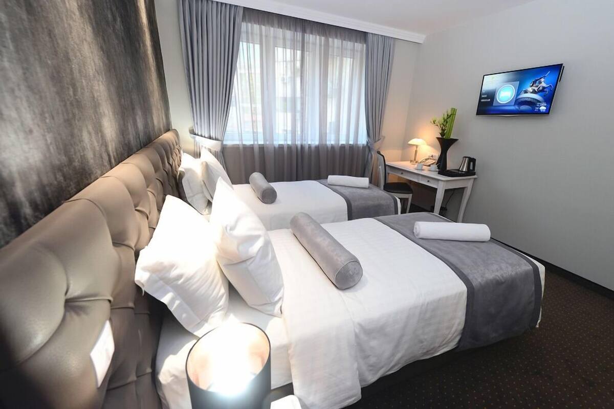 Une chambre d’hôtel avec deux lits, un canapé, un bureau avec une lampe et un téléviseur fixé au mur.