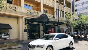 A white car parked in front of a building with a sign reading "ALEXANDAR SQUARE HOTEL".