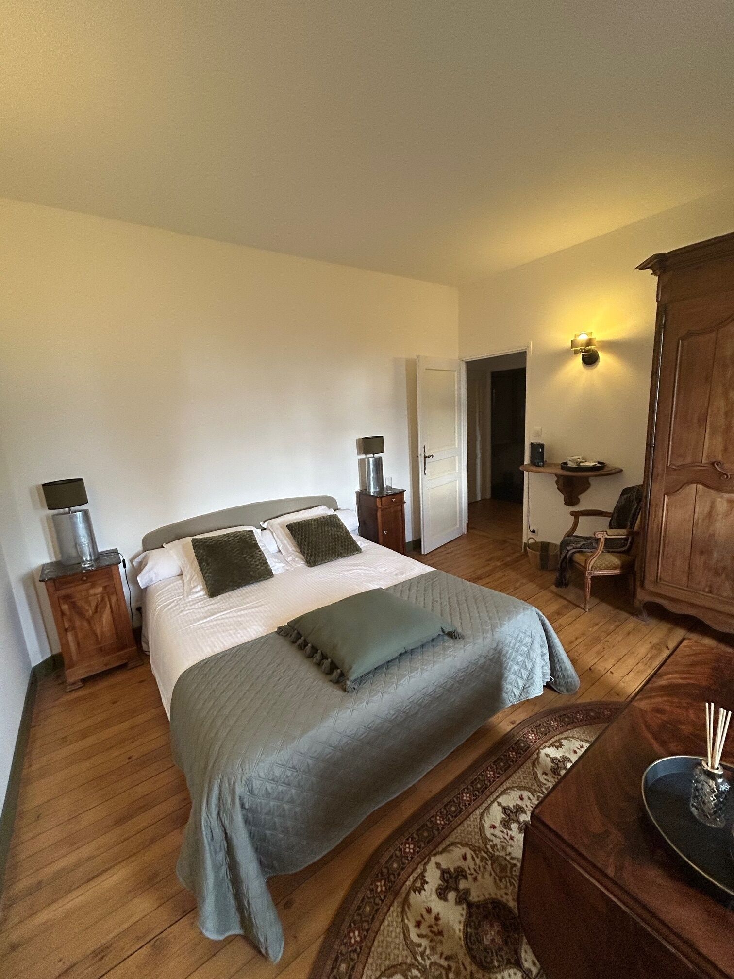 Une chambre à coucher comprenant un lit, des tables de chevet, une commode, une armoire en bois, une chaise, un bureau et une lampe.